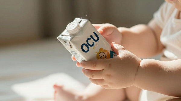 Manos de bebé sosteniendo leche artificial OCU.
