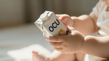 Manos de bebé sosteniendo leche artificial OCU.