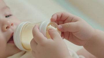 Bebé sosteniendo un biberón de leche de fórmula.
