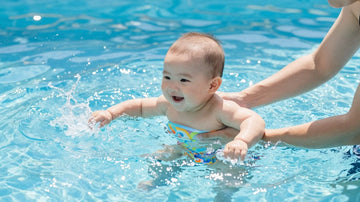 Bebé sonriendo en la piscina con un adulto.
