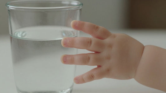 Bebé tomando agua de un vaso transparente.