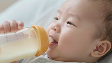 Bebé feliz con un biberón de leche hidrolizada.