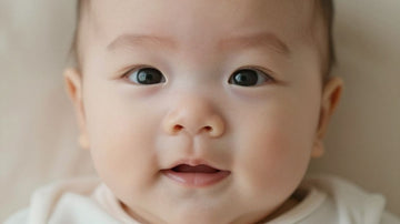 Bebé con expresión curiosa, luz suave, fondo pastel.