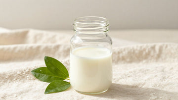 Biberón de cristal con leche y hojas verdes.