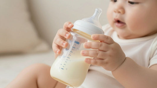 Bebé sosteniendo un biberón con leche.